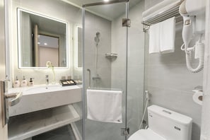 Et moderne badeværelse med en glasvæg omkring brusenichen, en hvid vask med spejl og et toilet.