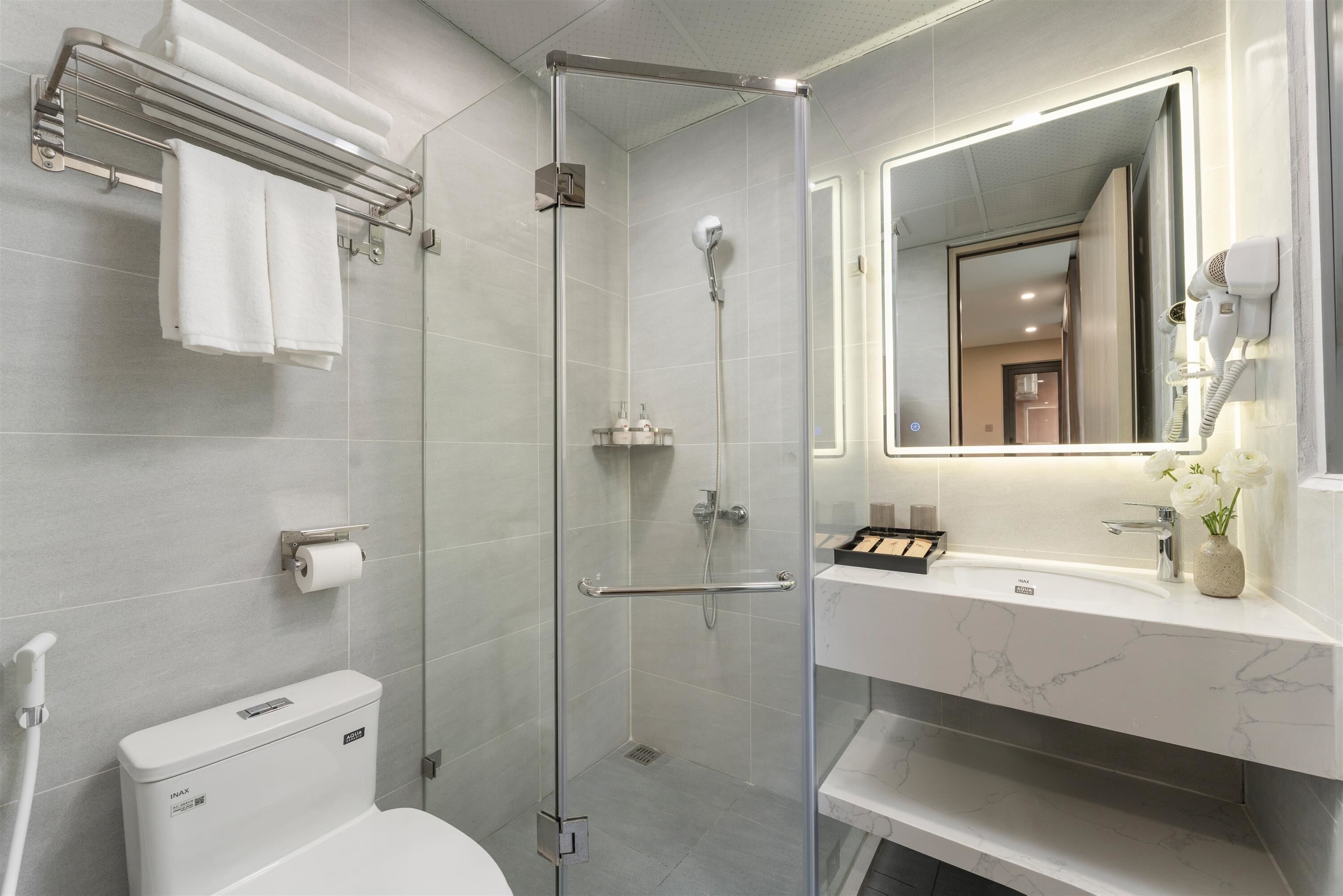A modern bathroom with a glass-enclosed shower, a toilet, a towel rack, and a vanity with a mirror.