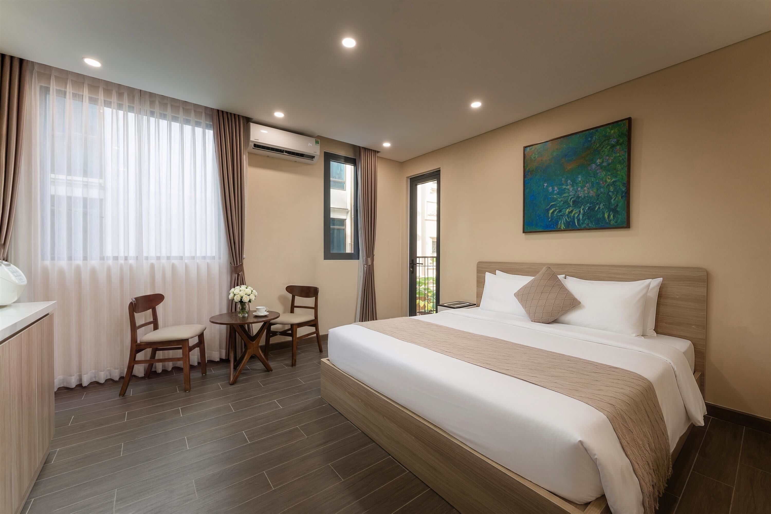 Ein Hotelzimmer mit einem großen Bett, einem Schreibtisch mit Stuhl, einem kleinen Tisch mit Blumenvase und einem Gemälde an der Wand.