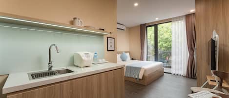 A hotel room with a kitchenette, a bed, a dining area, and a large window with curtains.