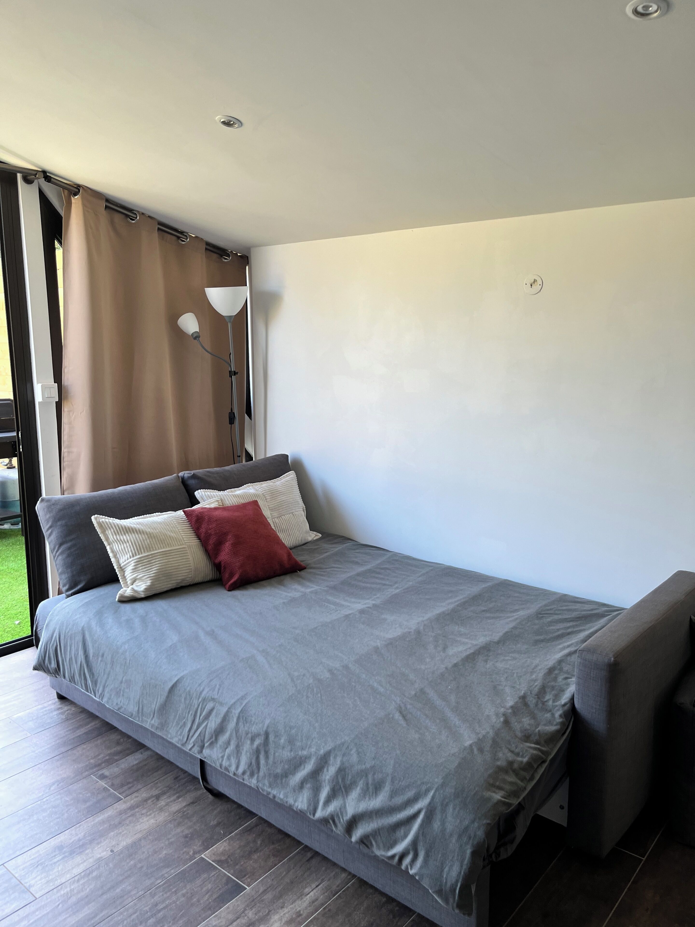 Une chambre à coucher moderne avec un lit gris, un oreiller rouge et un banc gris.