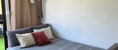 Un dormitorio moderno con una cama gris, un cojín rojo y un banco gris.