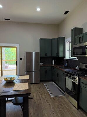 A modern kitchen with a stainless steel refrigerator, dark green cabinets, a gas stove, and a microwave. - Tall Pine Retreat — Cozy, Deep-Woods Getaway in tranquil Necedah (Necedah)