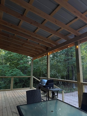 A covered outdoor area with a grill, seating, and a view of a forest. - Tall Pine Retreat — Cozy, Deep-Woods Getaway in tranquil Necedah (Necedah)