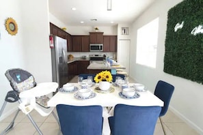 Un comedor con una mesa dispuesta para cuatro personas, una trona para bebé y una cocina al fondo.