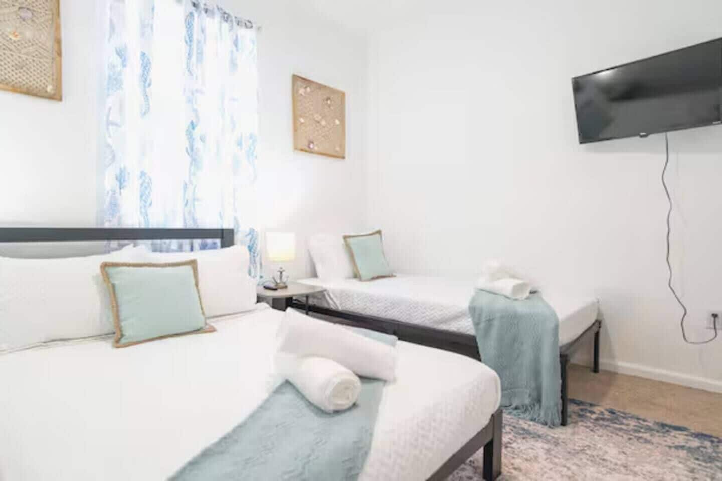 Une chambre d’hôtel avec deux lits, un téléviseur à écran plat fixé au mur et une fenêtre avec des rideaux.