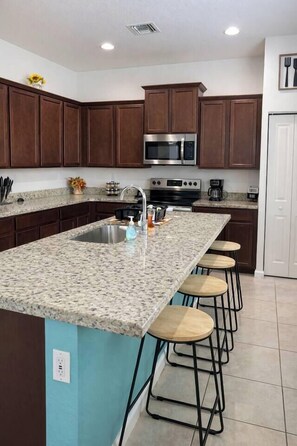 Una cocina con encimeras de granito, electrodomésticos de acero inoxidable y taburetes de bar de madera.