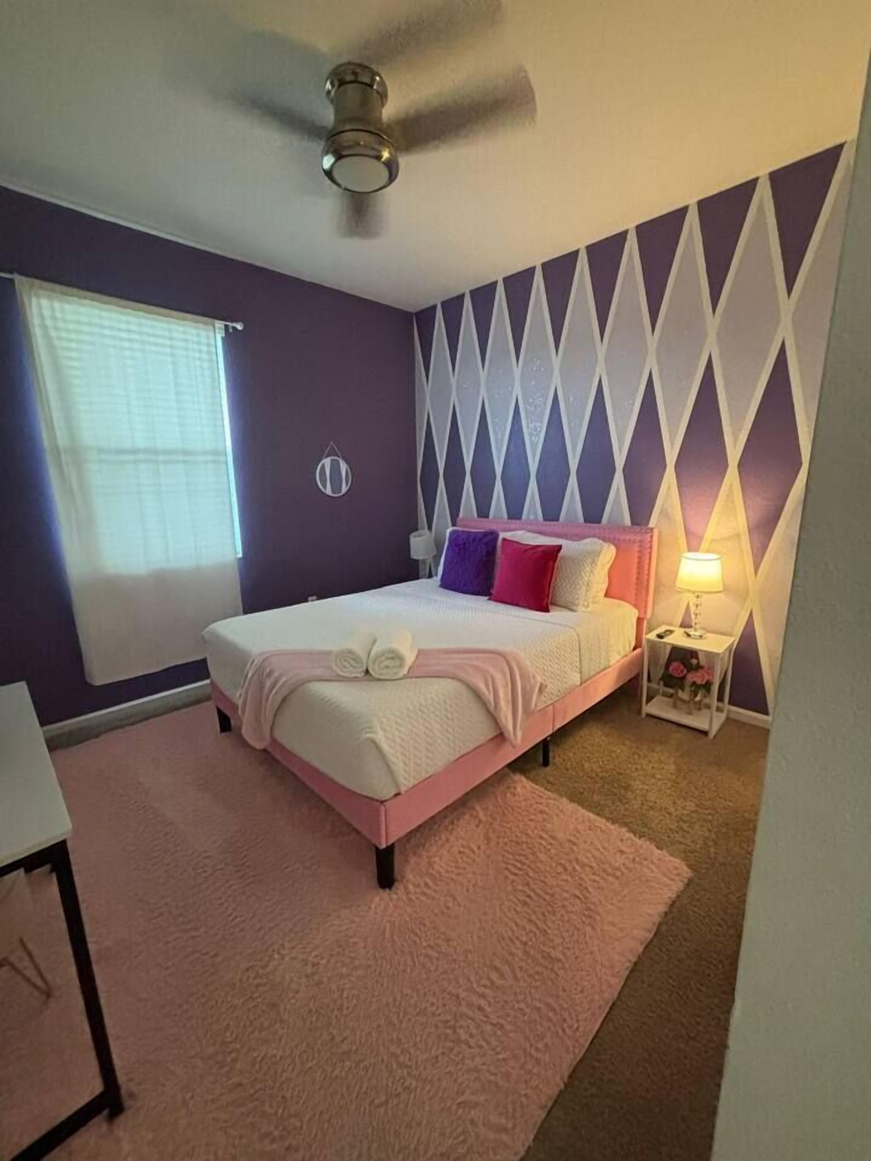 Une chambre à coucher avec un lit, un ventilateur de plafond, une table de chevet et une fenêtre avec des stores.