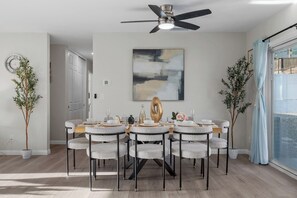 A dining area with a round table, eight chairs, a ceiling fan, and a large abstract painting on the wall.