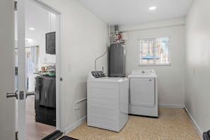 A laundry room with a washer and dryer, a water heater, and a window with blinds.