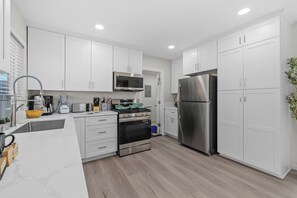 A modern kitchen with white cabinets, stainless steel appliances, and a wooden floor.
