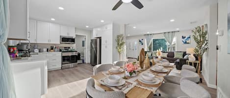 A modern kitchen with white cabinets, a central island, and a dining area with grey chairs and a wooden table set for six.