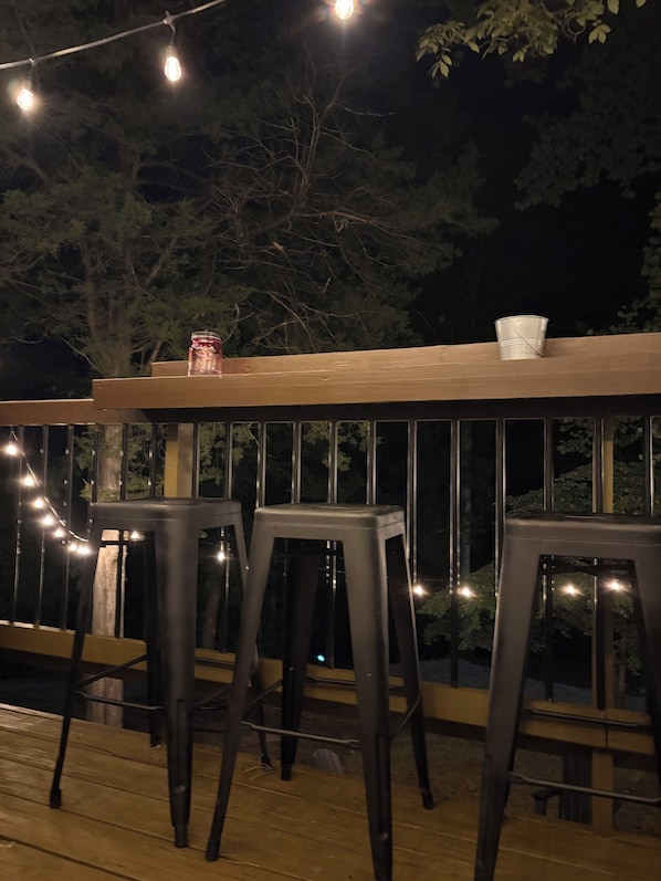 A deck with wooden railings, two black bar stools, and string lights.