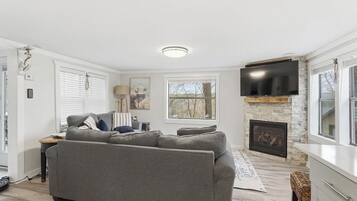 A living room with a grey sofa, a fireplace, a flat-screen TV, and a window with blinds.