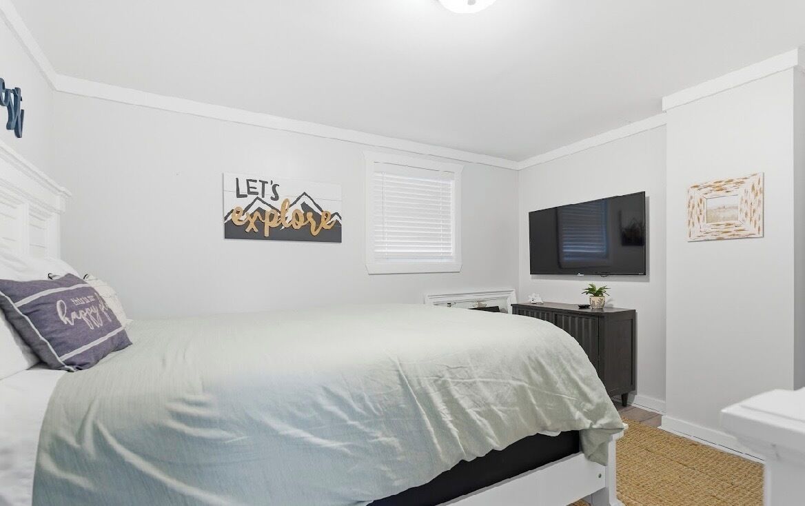 Une chambre à coucher avec un lit, un téléviseur fixé au mur, un radiateur et une petite plante posée sur la commode.