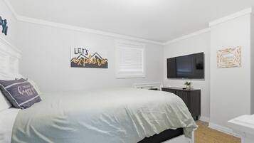 A bedroom with a bed, a TV mounted on the wall, a radiator, and a small plant on the dresser.