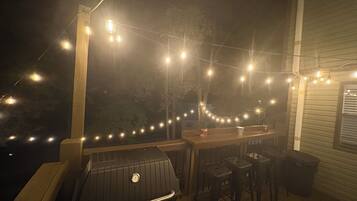 An outdoor deck with a barbecue grill, wooden chairs, and string lights.