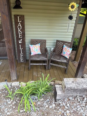 Een houten terras met twee houten stoelen, elk voorzien van een gebloemd kussen, en een houten bordje met de tekst 'LAKE LIF'.
