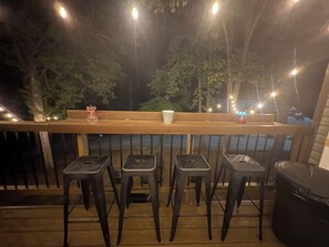 A wooden deck with a railing, four black stools, a bench, and string lights. - Make Memories at Center Hill Lake — Your Home Away From Home Family Friendly Fun (Smithville)