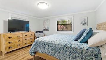 A bedroom with a bed, a TV, a wooden dresser, and a window with a view of trees.