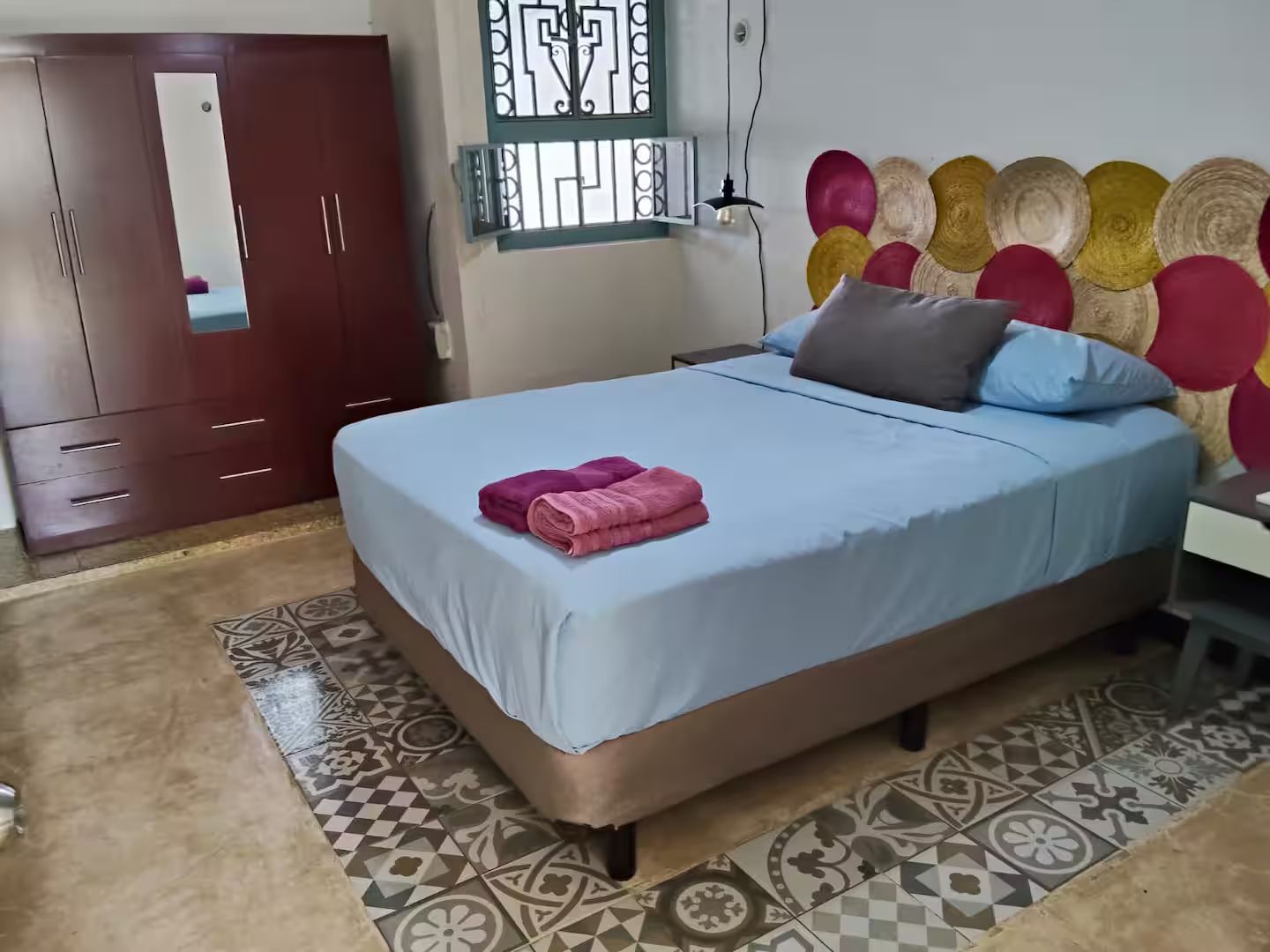 A bedroom with a bed, a wardrobe, a mirror, and a decorative wall panel.