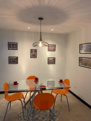 A dining area with a glass table, orange chairs, and framed pictures on the wall. - Casa FRIDA25 (Chelem)