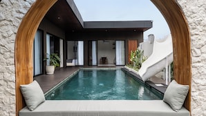 A pool with a wooden arch, a slide, and a modern building with large windows and a staircase.