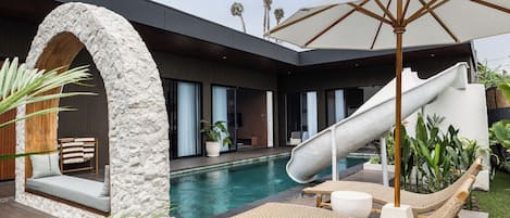 A modern house with a pool, a slide, and outdoor seating.