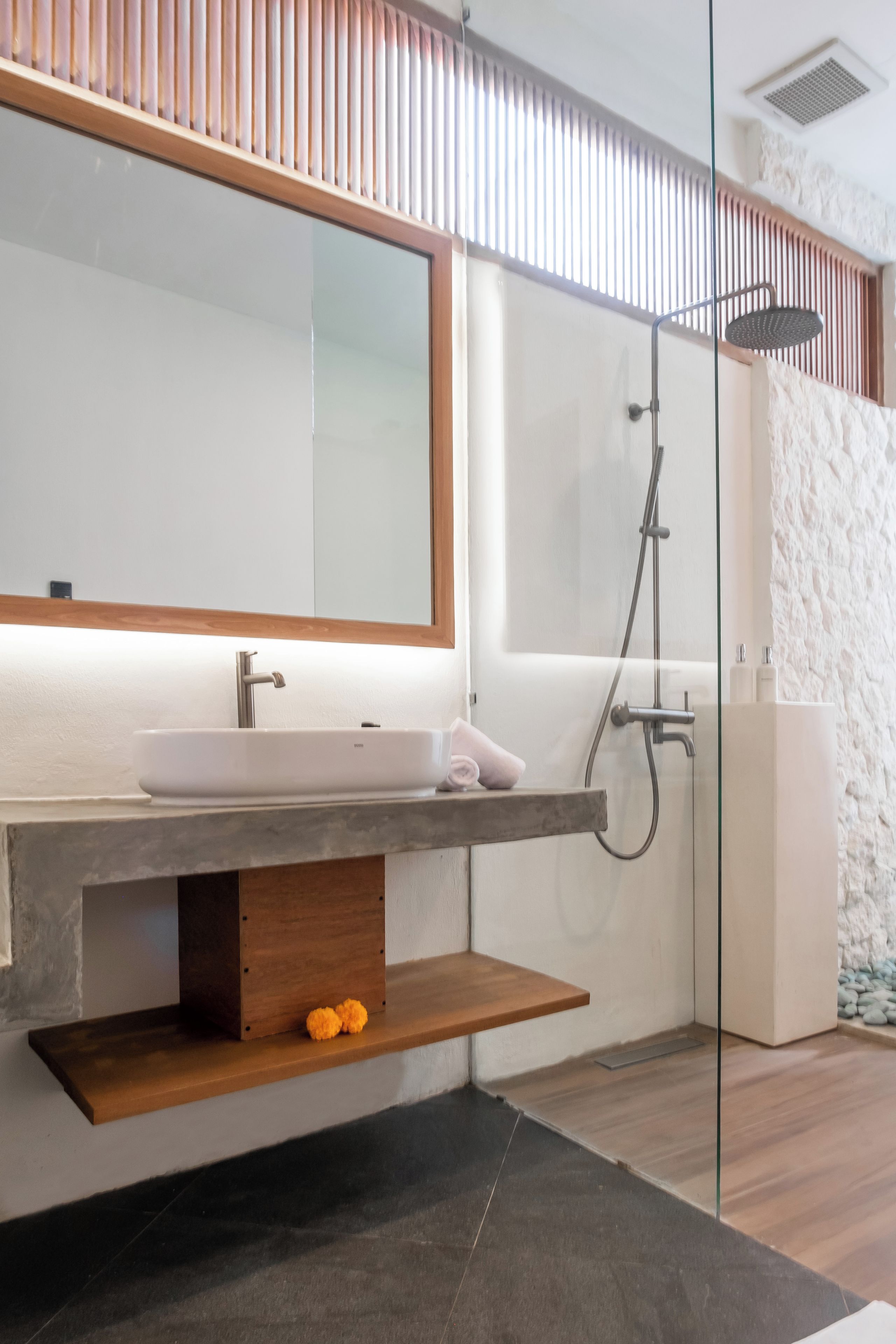 Un baño moderno con un espejo grande, un lavamanos empotrado, una ducha y un estante de madera.