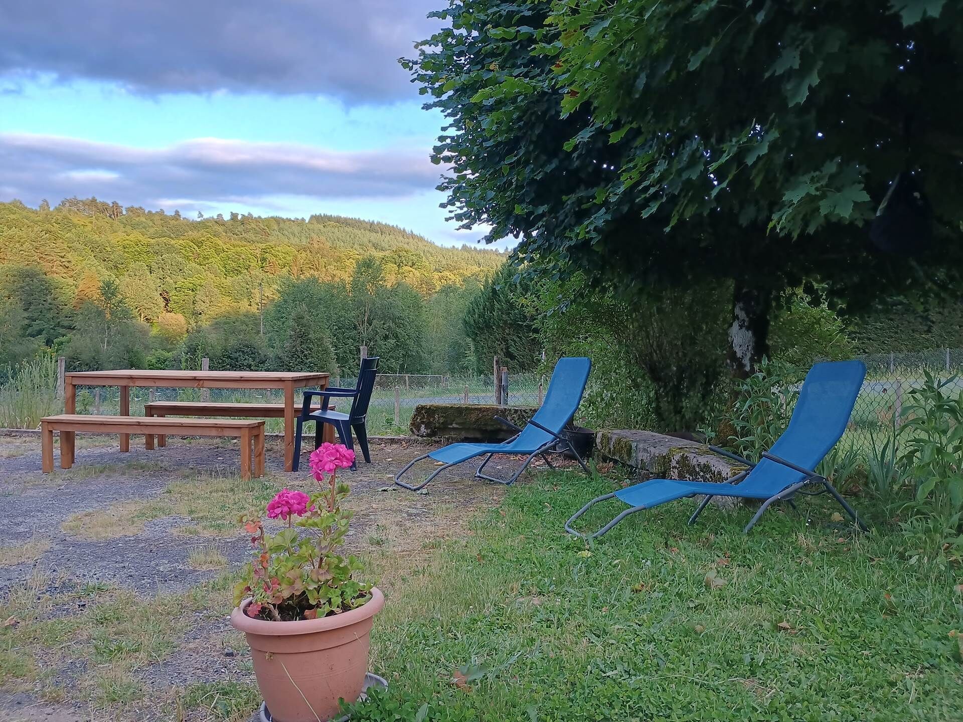 A garden area with a wooden bench, a table, and two blue lawn chairs.