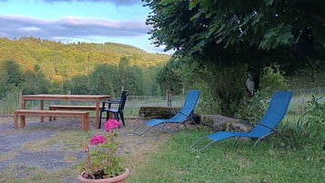 A garden area with a wooden bench, a table, and two blue lawn chairs.