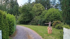 A gravel driveway leading to a gated area with a wooden sculpture.