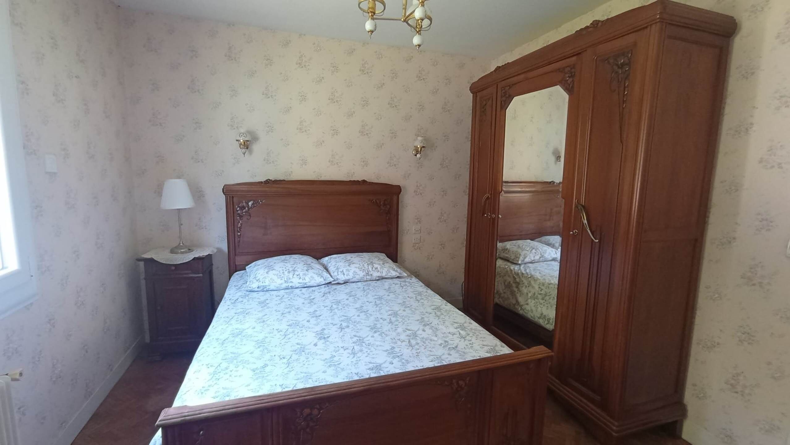 Ein Schlafzimmer mit einem hölzernen Bett, einem Nachttisch, einer Lampe und einem Kleiderschrank.