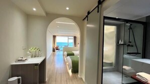 Corredor moderno de hotel com vista para o mar, uma área de estar com almofada verde e um espaço com chuveiro.
