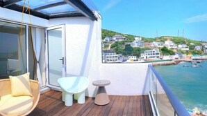 Un balcone con una sedia in vimini, un tavolino e vista su una località costiera.