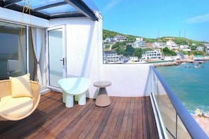 A balcony with a wicker chair, a small table, and a view of a coastal town. - Dongji Inter national Youth Hostel (Zhoushan)