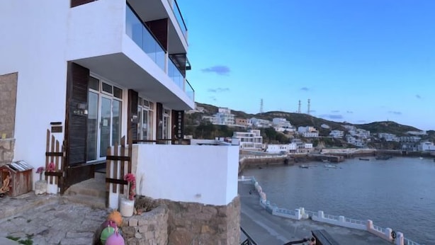 Um edifício à beira-mar com varanda e vista para o mar, uma parede de pedra e a linha costeira.