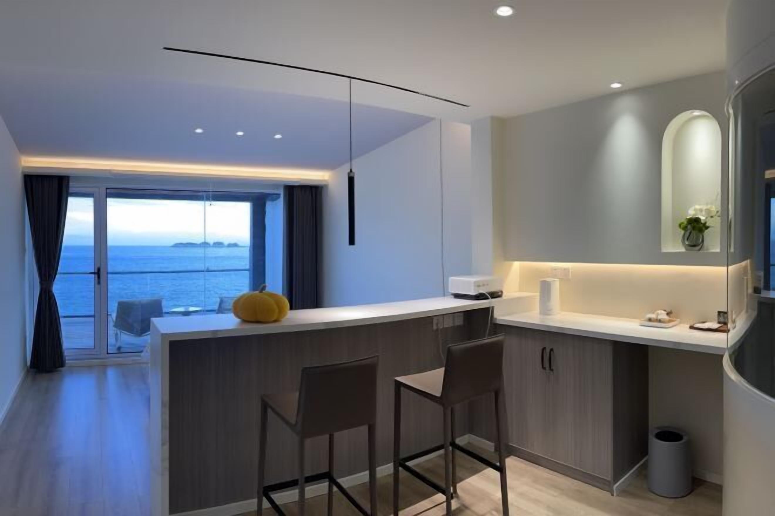 A modern kitchen with a central island, bar stools, and a view of the sea.