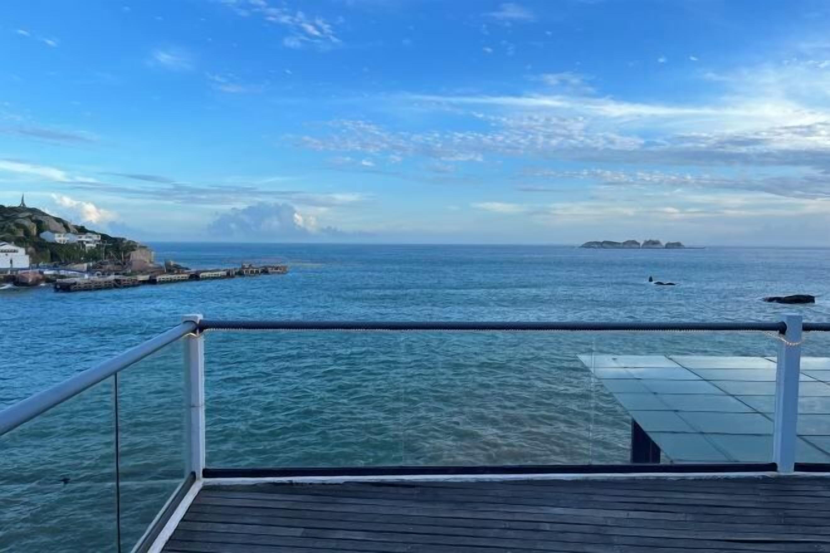 Une vue prise depuis le pont d’un navire, avec une rambarde, une mer calme et une terre lointaine parsemée de bâtiments.
