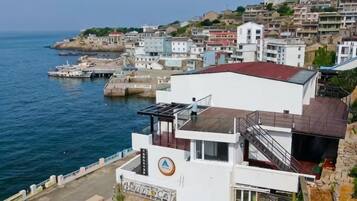 A coastal building with a white facade, a red roof, and a staircase leading to an upper level.