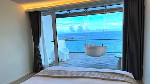 Una camera d'hotel con un letto, vista mare e un balcone con una poltrona amaca.