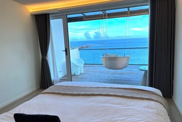 A hotel room with a bed, a view of the sea, and a balcony with a hanging chair. - Dongji Inter national Youth Hostel (Zhoushan)