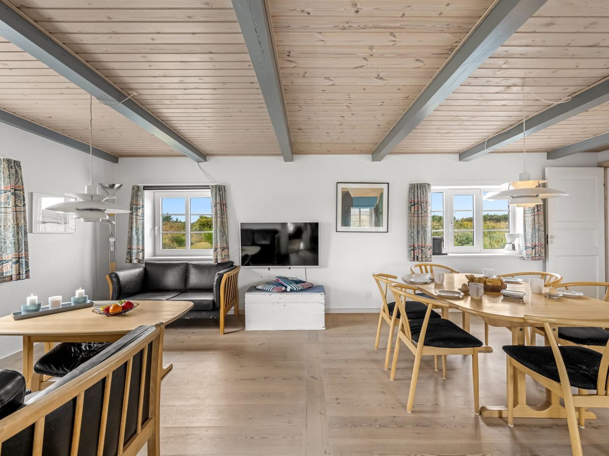 Una sala de estar moderna con techo de madera, un sofá, una mesa de comedor con sillas y un televisor montado en la pared.