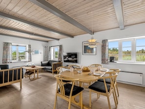 Un comedor amplio con una mesa y sillas de madera, un televisor y ventanas grandes que ofrecen vistas al exterior.