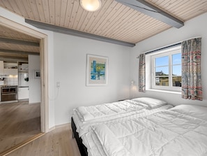 Un dormitorio con una cama grande, una ventana con cortinas, un cuadro en la pared y vistas a la cocina y el salón.