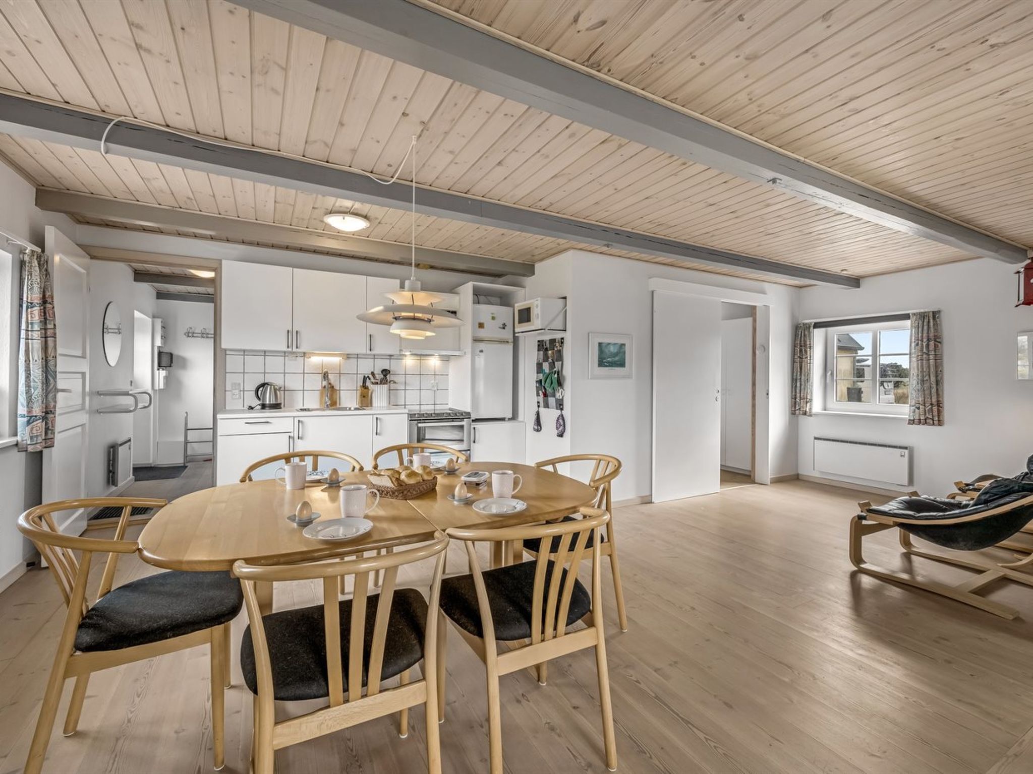 Eine moderne Küche mit weißen Schränken, ein Essbereich mit einem Holztisch und Stühlen sowie ein großes Fenster mit Blick.