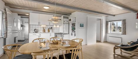 A modern kitchen with white cabinets, a dining area with a wooden table and chairs, and a large window with a view.