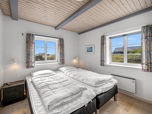A bedroom with two beds, a nightstand, a window with curtains, a wall-mounted light, and a framed picture.