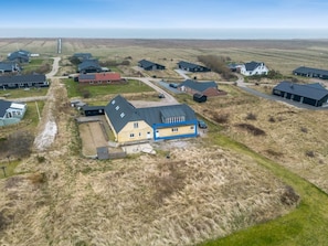 Zona rural con varias casas, un edificio grande amarillo con sección azul y una vista despejada del horizonte.