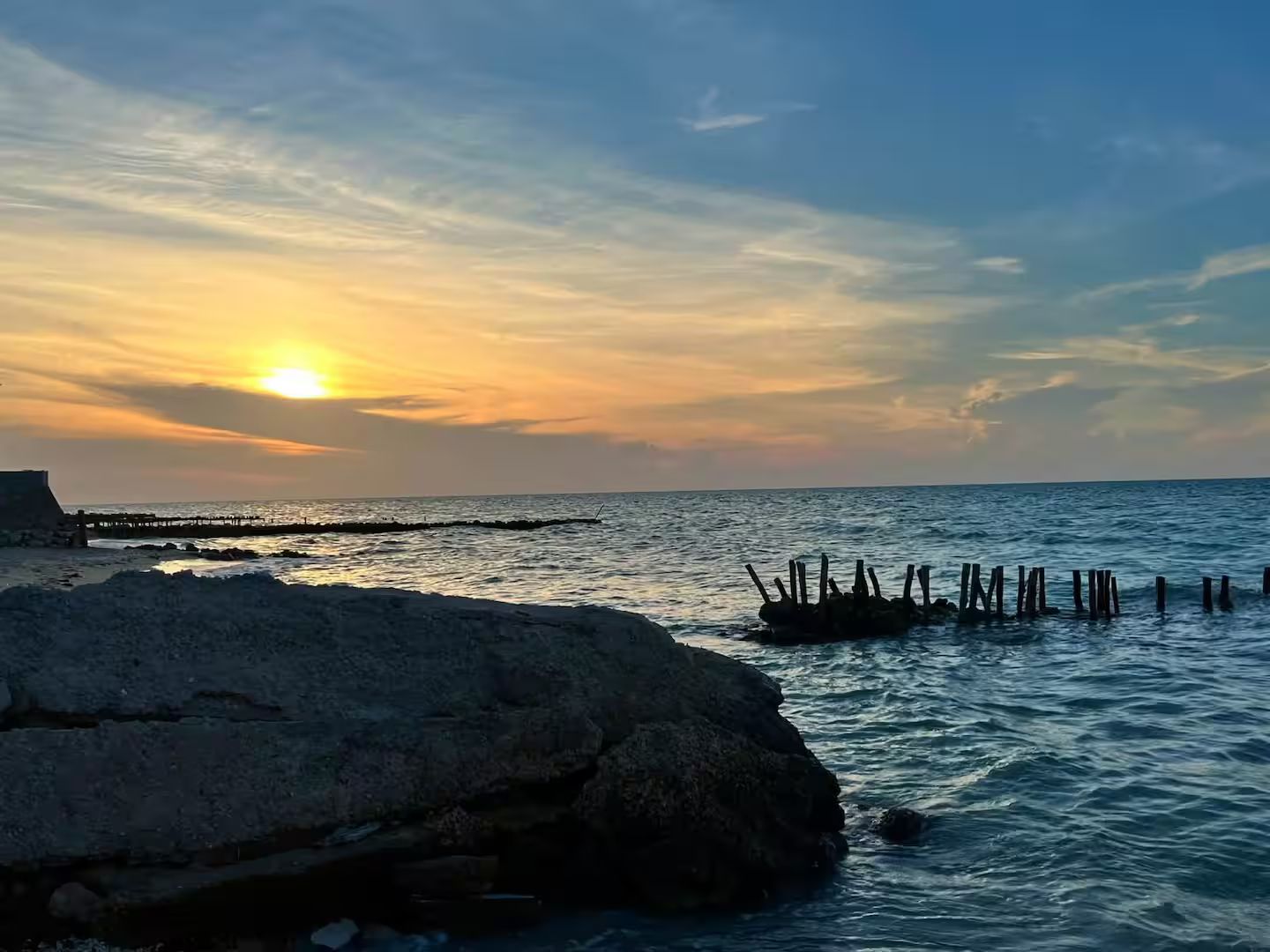 A coastal sunset with rocky terrain and a pier extending into the sea.